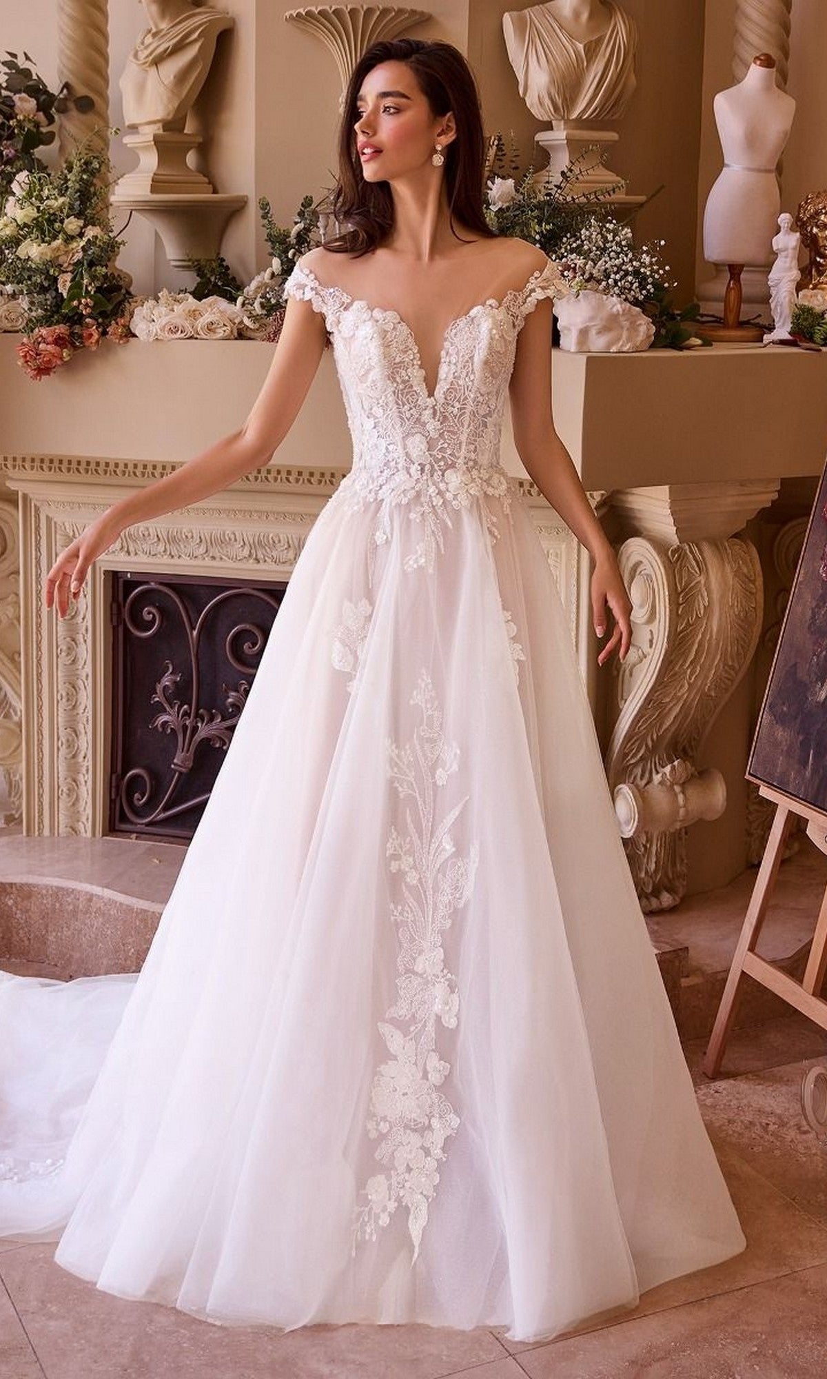 A woman wearing the Andrea and Leo WL038 Long Wedding Dress stands in an elegant room adorned with classical decor and floral arrangements.